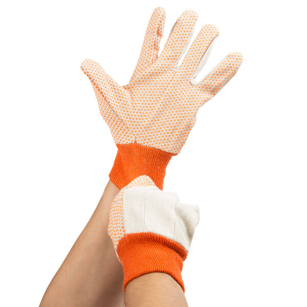 A person wearing Cordova cotton canvas work gloves with orange PVC dotted palms.