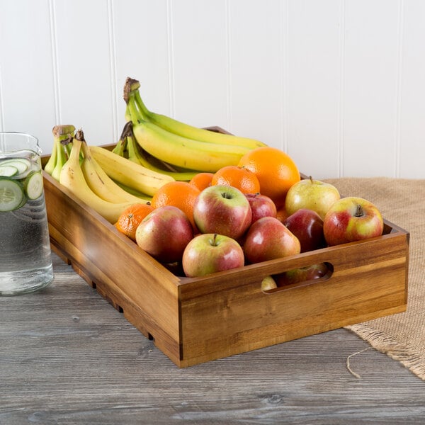 A Tablecraft acacia wood crate filled with a variety of fruit on a table with a glass of water.