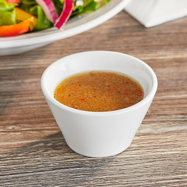 An Acopa bright white sauce cup filled with brown liquid on a table in front of a plate of food.