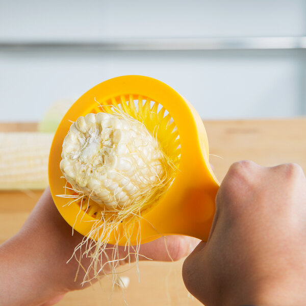 A person's hand using a Weston Desilker Corn Brush to grate corn over a bowl.