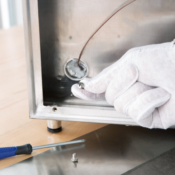 A person in a white Cordova cotton glove using a screwdriver to repair a metal object.