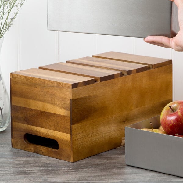 A hand holding a Tablecraft acacia wood serving crate with red apples inside.