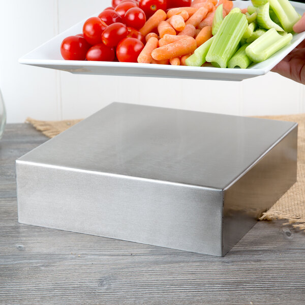 A plate of vegetables and tomatoes on a Tablecraft stainless steel square bowl.