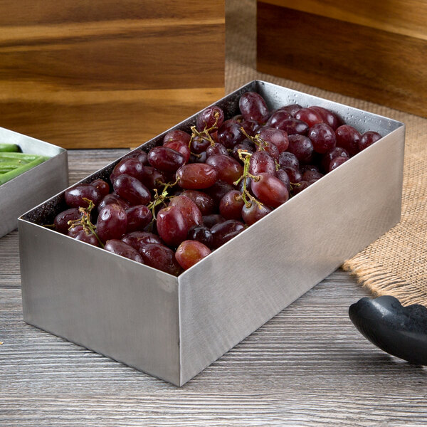 A Tablecraft stainless steel rectangular bowl full of grapes on a counter.