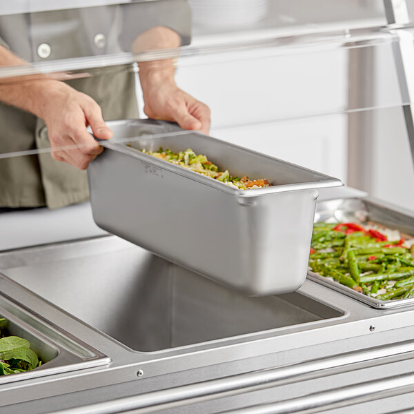 A person holding a Vollrath stainless steel steam table pan full of food.