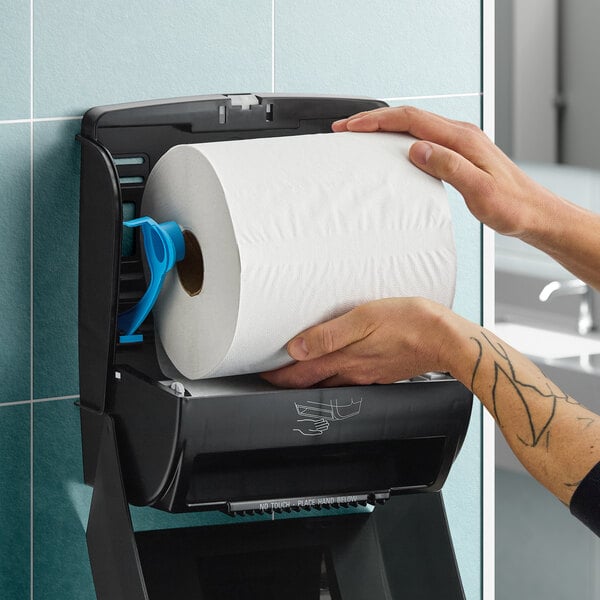 A large white hardwound paper towel roll being loaded into a black wall-mounted dispenser.