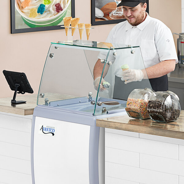 An Avantco flat glass sneeze guard on a counter with a glass case.