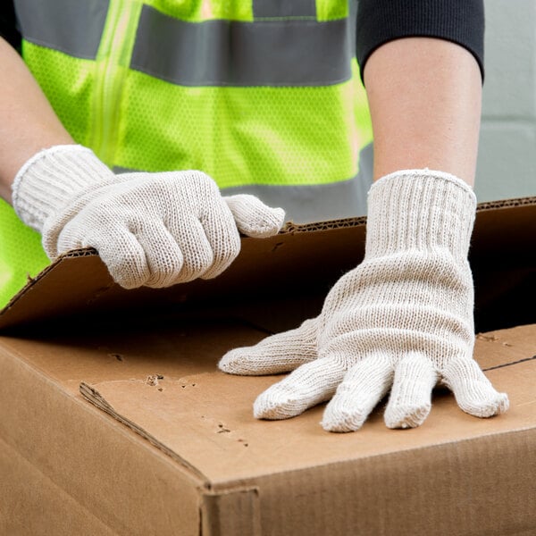 A person wearing Cordova economy weight natural polyester/cotton work gloves holding a cardboard box.