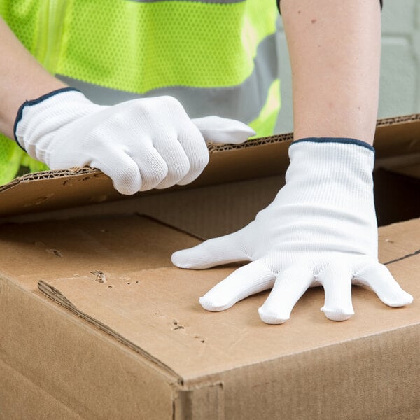 A pair of white nylon work gloves being worn by a person handling a cardboard box.
