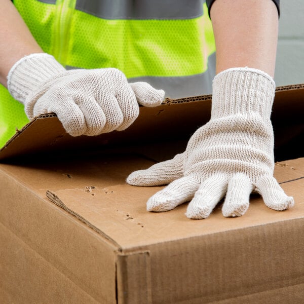 A person wearing Cordova lightweight natural polyester/cotton work gloves opening a cardboard box.