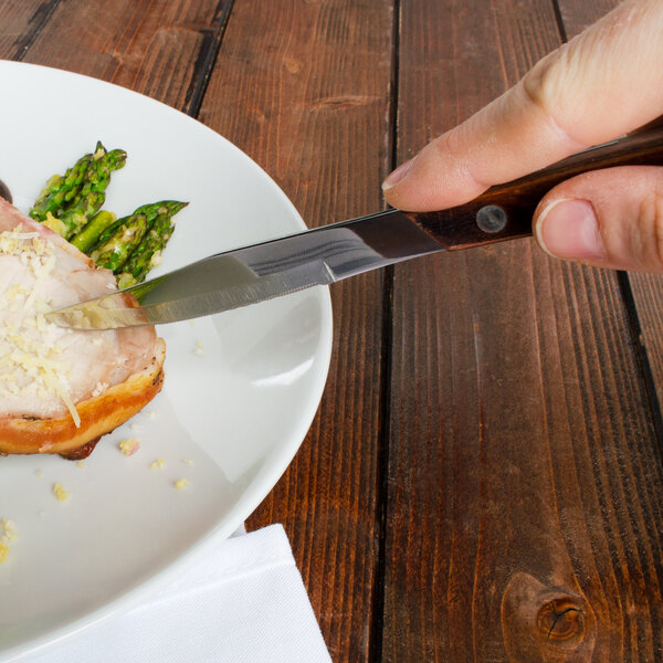 A person using a Walco steak knife to cut food on a plate.