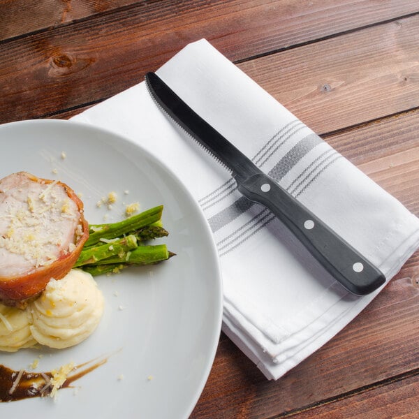 A Walco stainless steel steak knife on a plate with food.