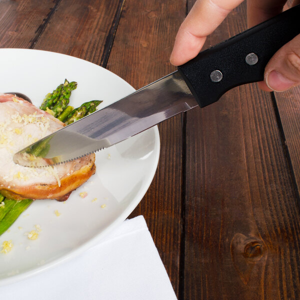 A person using a Walco stainless steel steak knife to cut a piece of meat.