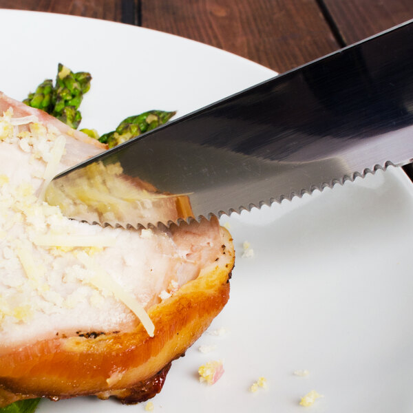 A Walco steak knife with a jumbo plastic handle cutting a piece of meat.