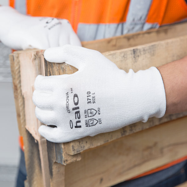 A pair of white Cordova Halo HPPE/synthetic fiber gloves with white polyurethane palm coating being worn while handling a wooden pallet.