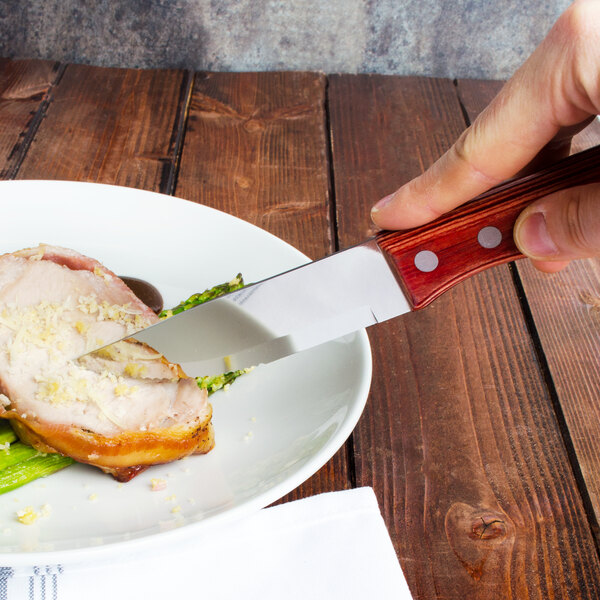 A person cutting a piece of meat on a plate with a Walco Big Red steak knife.