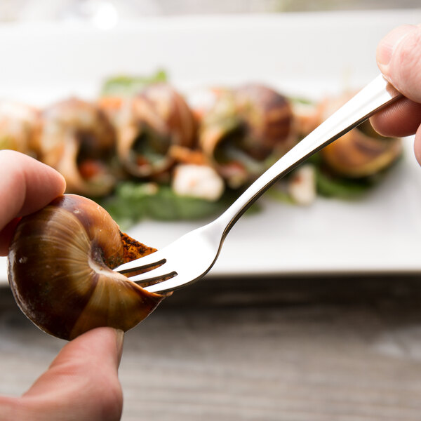 A hand holding a Walco Lancer cocktail fork with a snail shell.