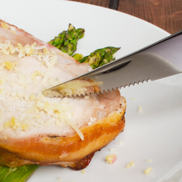 A Walco stainless steel steak knife cutting a piece of meat with asparagus.