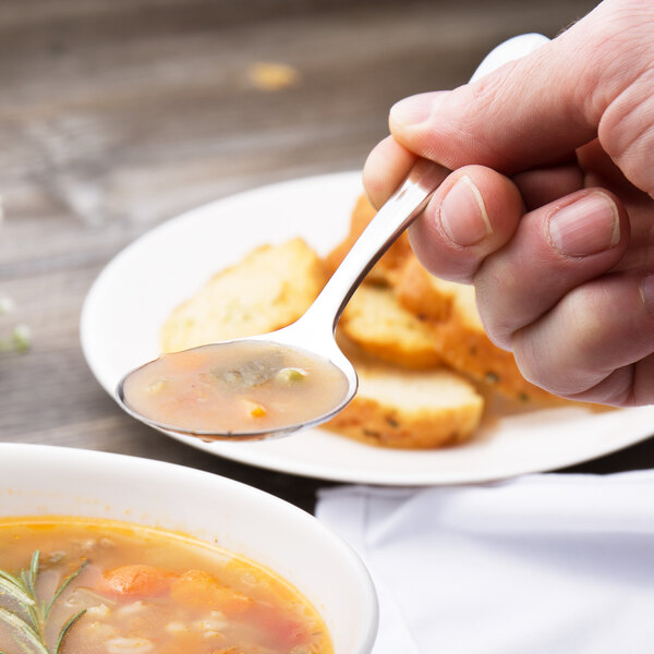 A person using a Walco Lancer stainless steel bouillon spoon to eat soup.