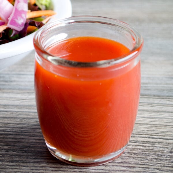 A glass of red liquid next to a bowl of salad in a Acopa round glass sauce cup.