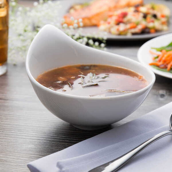 A Villeroy & Boch white porcelain bowl of soup with a spoon and fork on a table.
