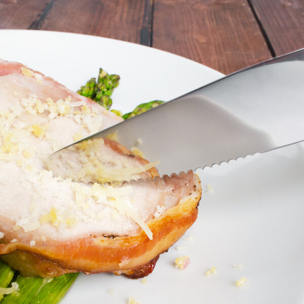 A Walco stainless steel steak knife cutting food on a plate.