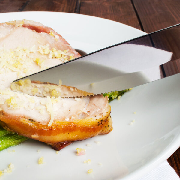 A Walco stainless steel steak knife cutting meat on a plate.