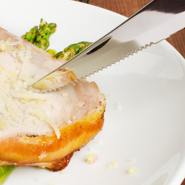 A Walco Parisian steak knife cutting a piece of meat with asparagus.