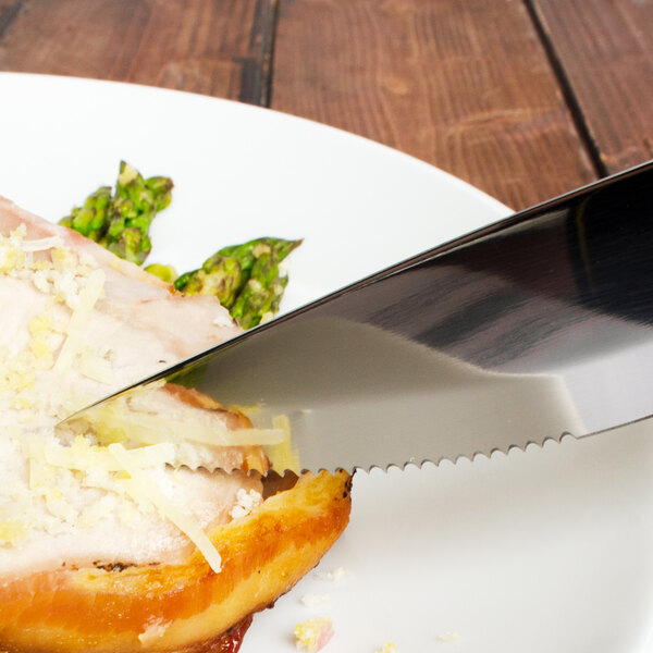 A Walco stainless steel steak knife cutting a piece of bread with cheese on a plate.