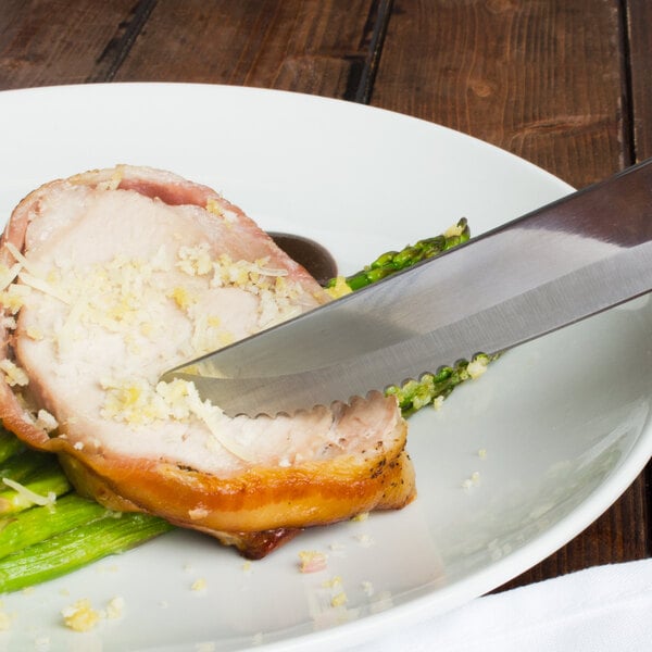 A Walco Denver steak knife cutting a piece of meat on a plate.
