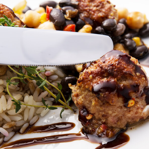 A Walco stainless steel dinner knife in a plate of food with meatballs and rice.