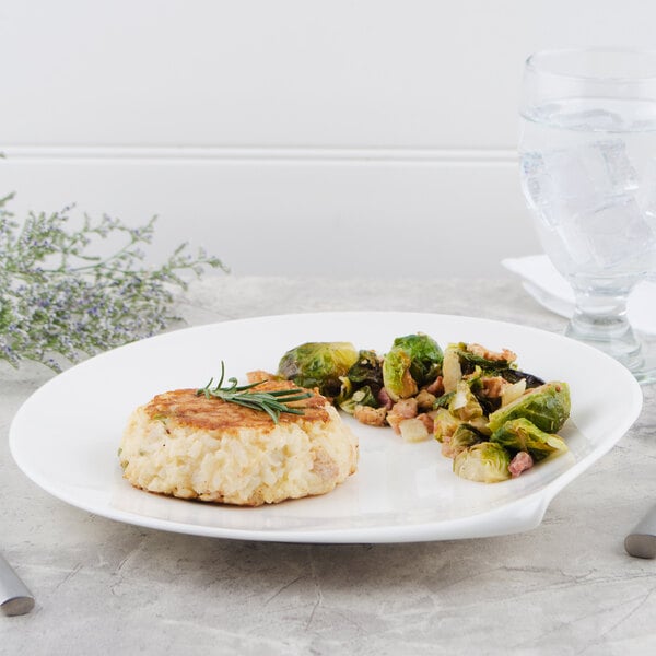 A Villeroy & Boch white porcelain flat plate with a crab cake and brussels sprouts on a table with a glass of ice water.