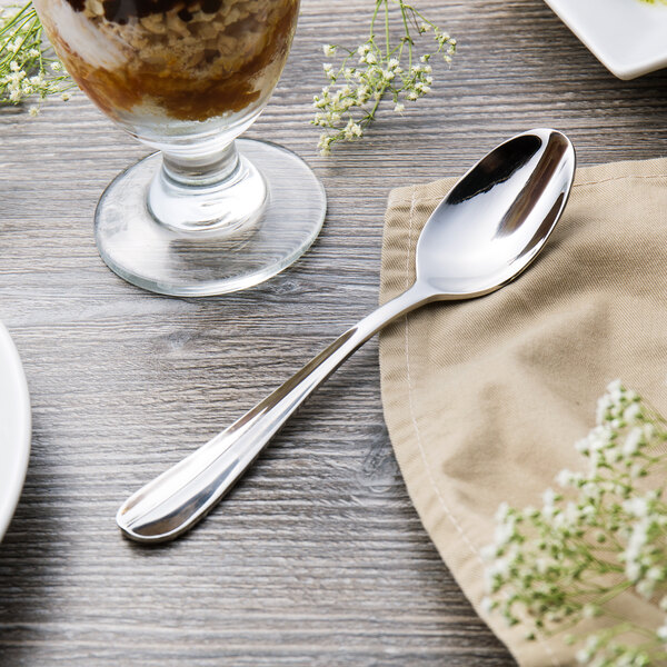 A Walco Lancer stainless steel dessert spoon on a napkin next to a glass of milk.