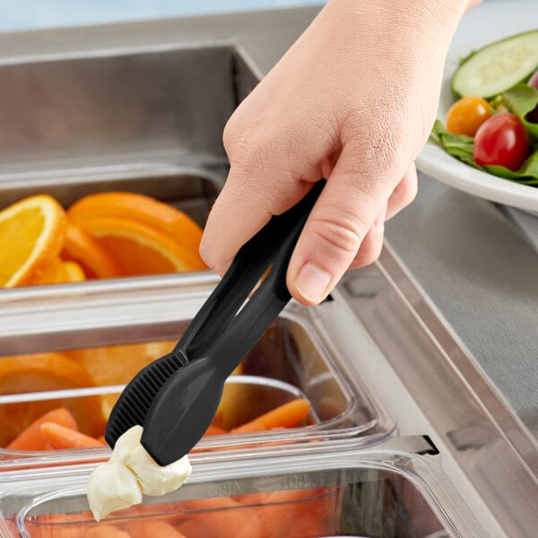 A hand holding a black Cambro Lugano plastic tong over a salad