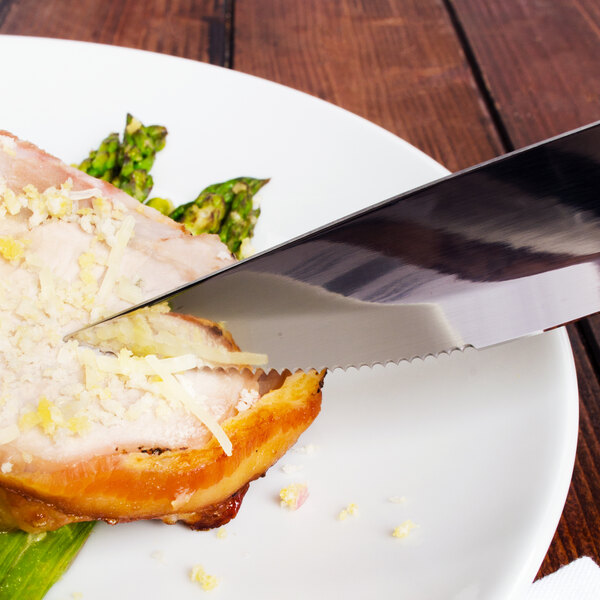 A Walco steak knife cutting a piece of meat on a plate.