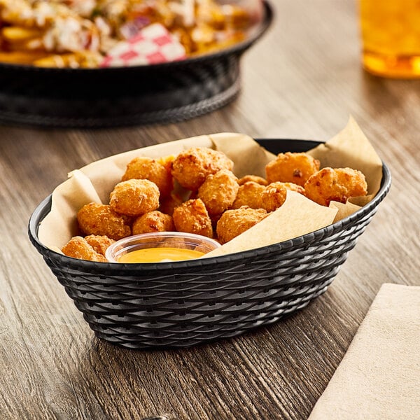 A Carlisle black plastic oval serving basket filled with fried chicken on a table.