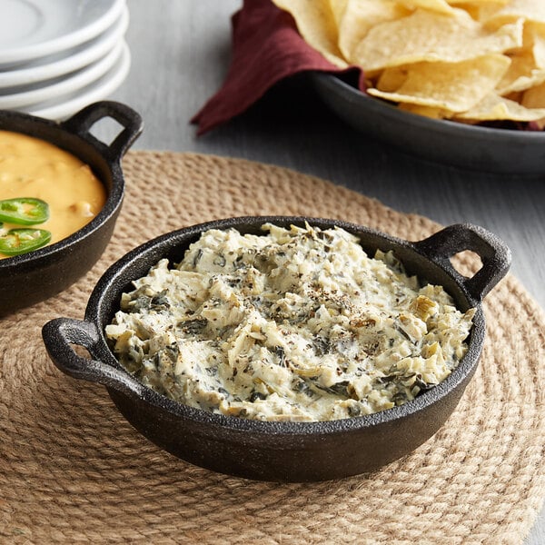 A Valor pre-seasoned mini cast iron round casserole dish filled with dip and chips on a table.