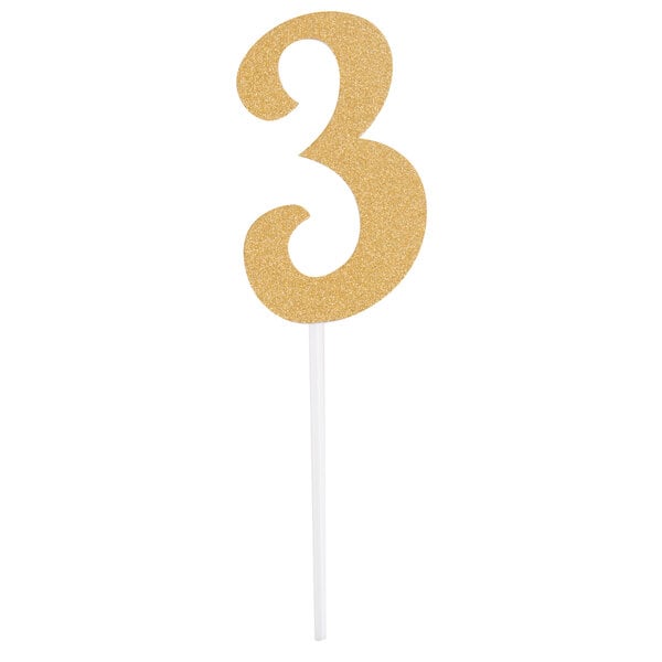 A gold glittery "3" cake topper on a white stick.
