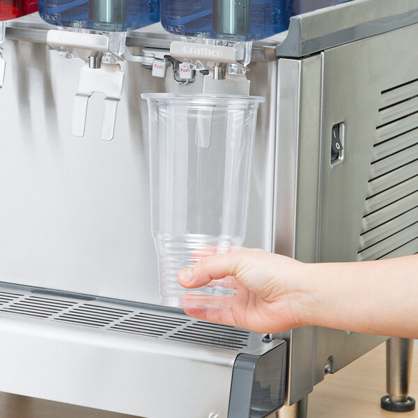 A hand holding a clear plastic cup of water under a Crathco beverage dispenser.