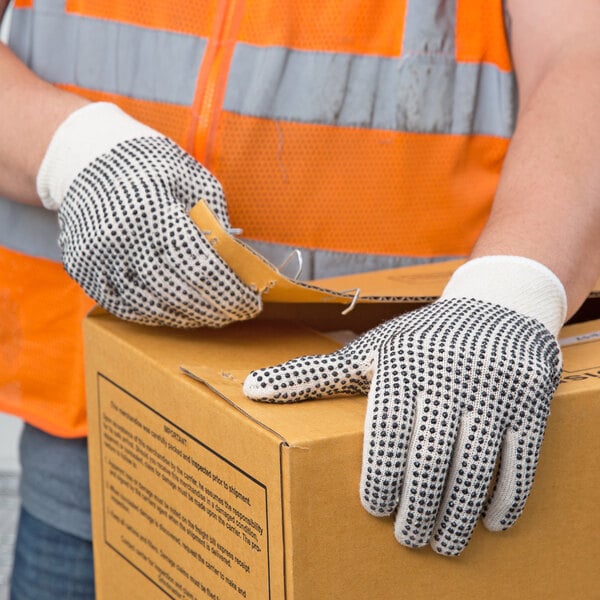 A person wearing Cordova gray work gloves with black PVC dots holding a box.