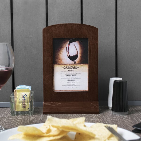 A Menu Solutions walnut wood menu frame on a table with chips and a glass of wine.