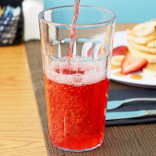 A person pouring red liquid into a Cambro plastic tumbler on a table.