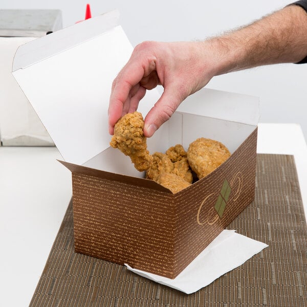 A hand holding a piece of fried chicken in a Hearthstone take-out box.