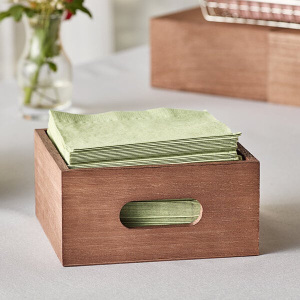 A brown wooden display crate with a stack of green napkins inside.