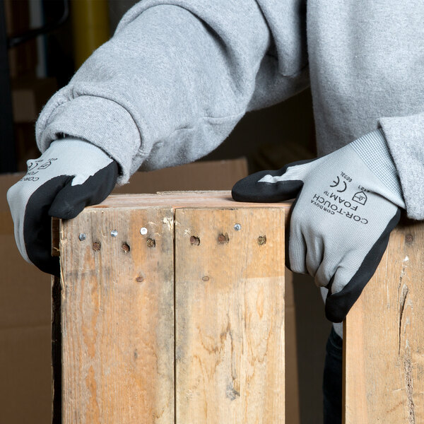 A person wearing Cordova gray nylon gloves with black foam nitrile palm coating holding a piece of wood.