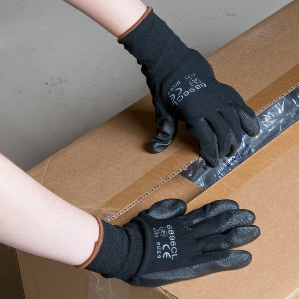 A person wearing Cordova black nylon gloves with black polyurethane palm coating opening a box.