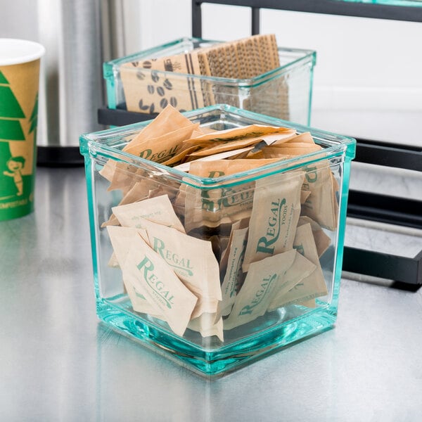 A clear square Cal-Mil glass jar with brown packets inside.