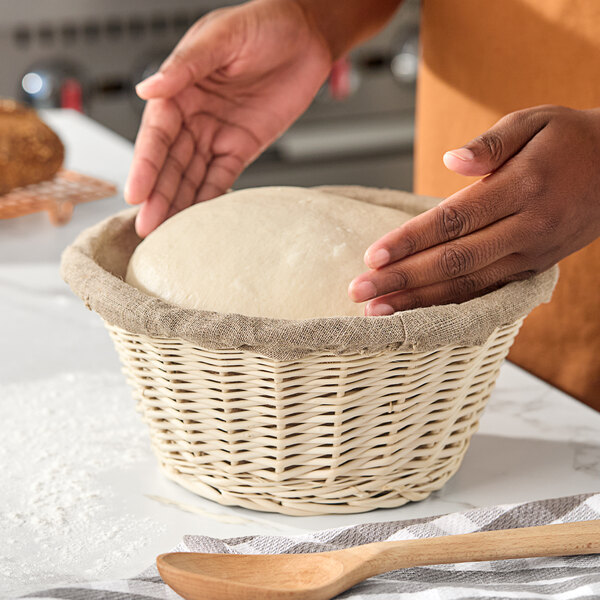A round wicker proofing basket lined with linen, containing dough being prepared for baking.