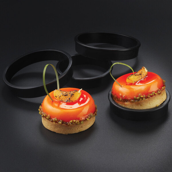 A group of round pastries with orange glaze and fruit on top in a bakery display.