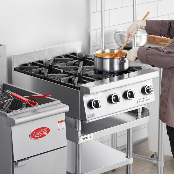 A woman using a Garland countertop range to cook food in a metal pot.